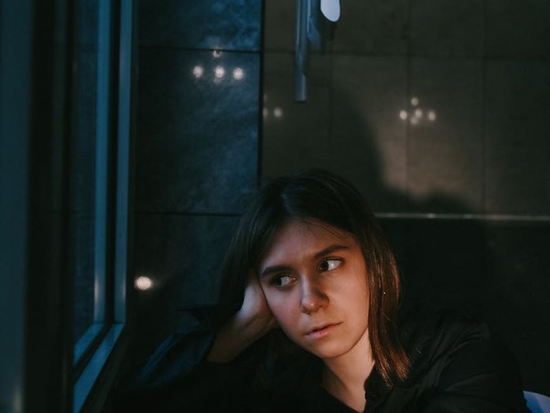 Person sitting calmly in a well-lit room, looking out a window.